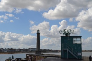 Four bikes leap from a central point, like the cardinal points of a compass, from the roof of the Harbour Arm Lookout.  Across the harbour in the distance is Margate