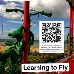 Two children's bikes about to leap from a balcony, with title, logos & QR code