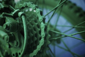 close of green painted chain and gear wheel, with the bike wheel in the background